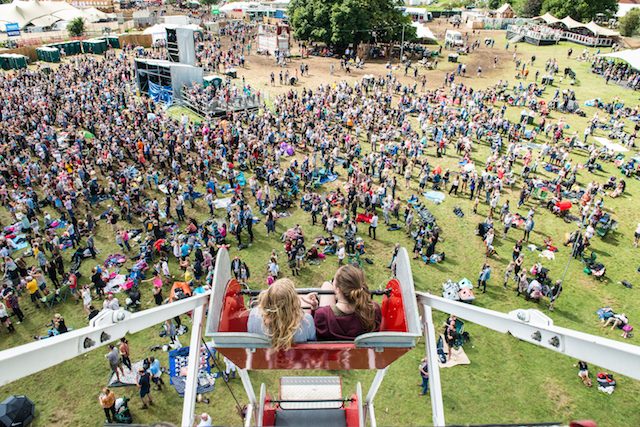 Two girls on ferris wheel, aerial shot showing festival crowds below